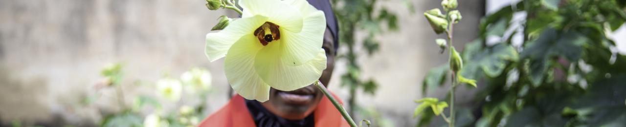 A woman holds a yellow flower to hide her face.