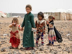 Four young Yemeni girls holding hands in front of the camp. Two of younger girls eating food items delivered by WFP